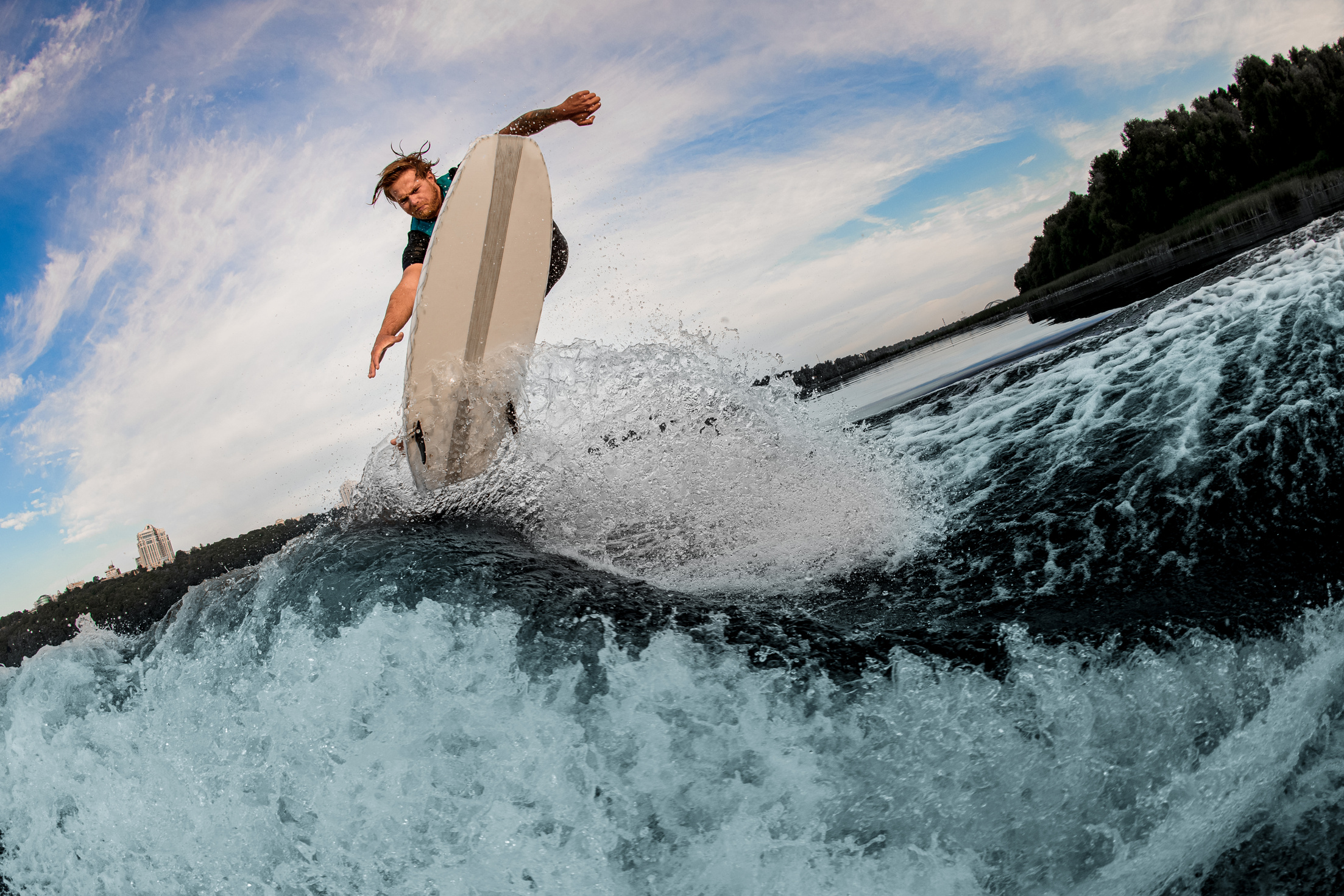 Active guy wakesurfer jumping on a wakesurf board over splashing river waves